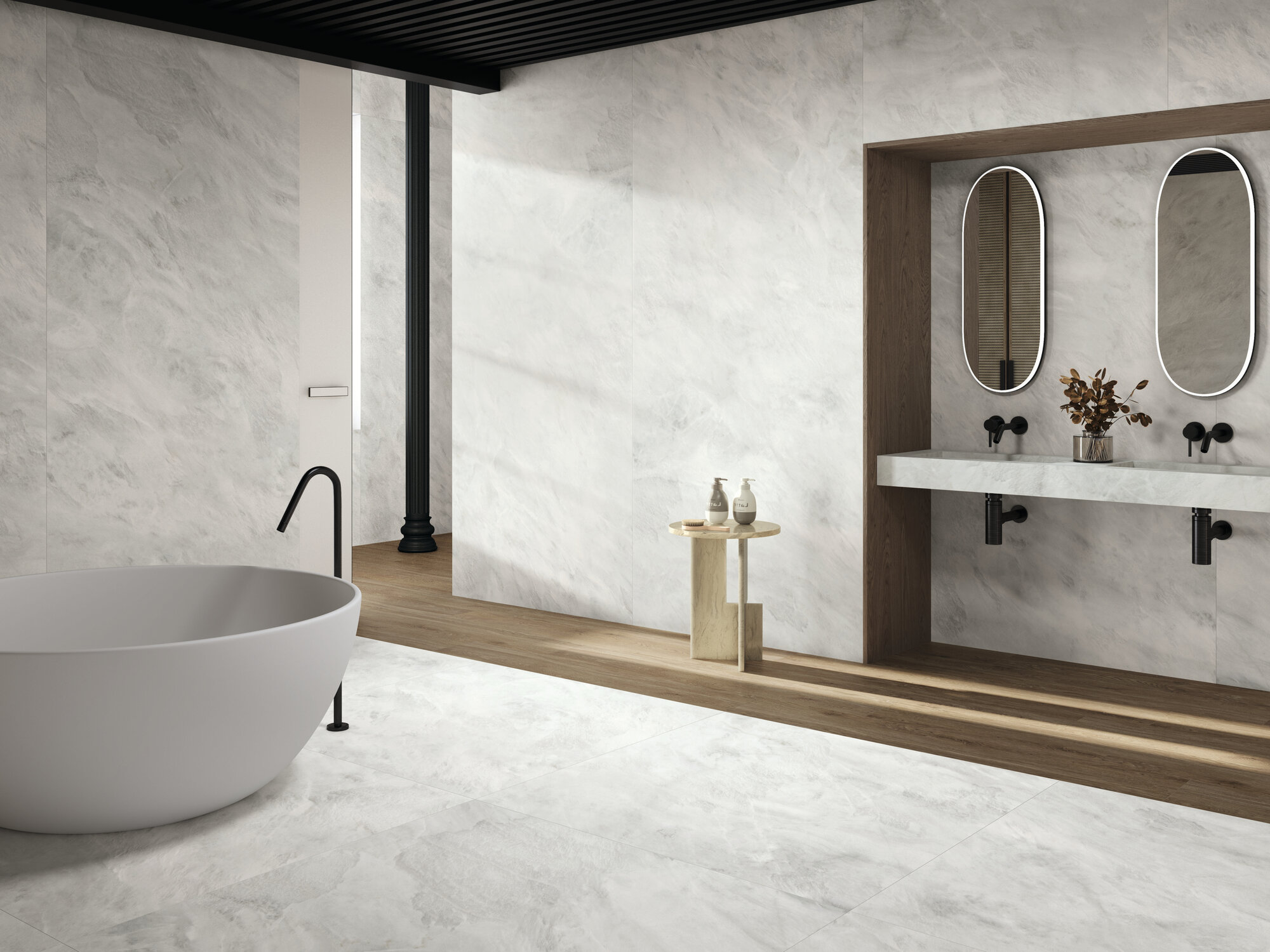 Bathroom with soft grey-white marble tiles, freestanding bathtub and twin oval mirrors over a wooden bench, Alexandria collection